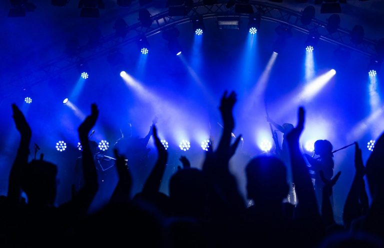 Eventplanung Hände von begeistertem Publikum bei einem Konzert, umgeben von blauen Lichtstrahlen.